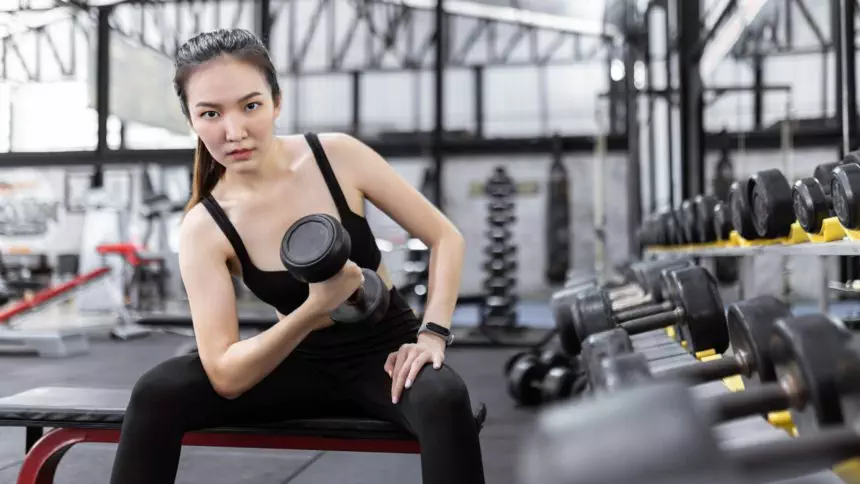 lady paying attention on carrying a dumbbell with her right hand while sitting on the bench